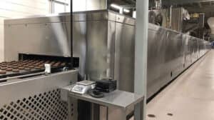conveyer belt with cookies coming out of a large machine on a factory floor