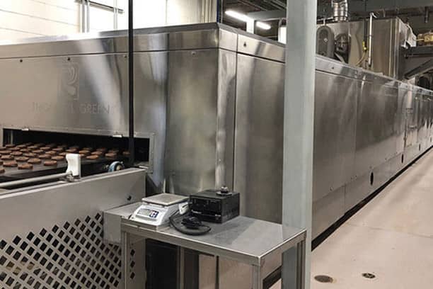 conveyer belt with cookies coming out of a large machine on a factory floor